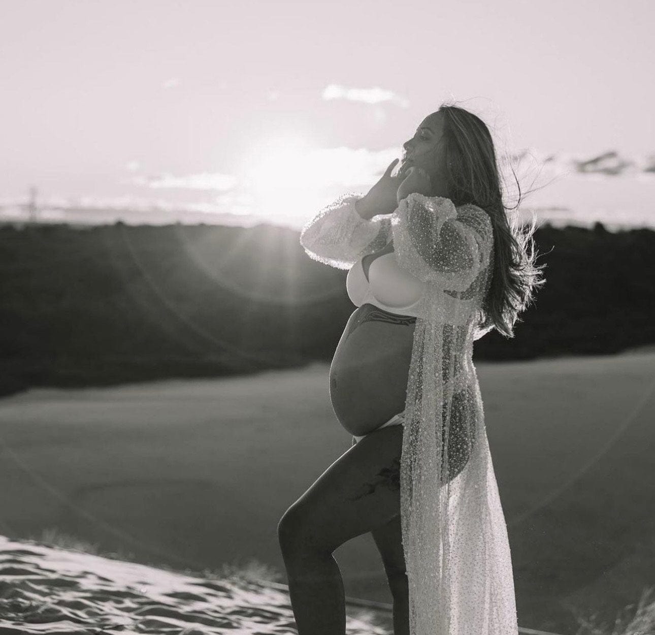 A pregnant lady stands on the sand dunes holding her face wearing Everything Lace Hire Athena Sparkly beaded maternity photoshoot robe