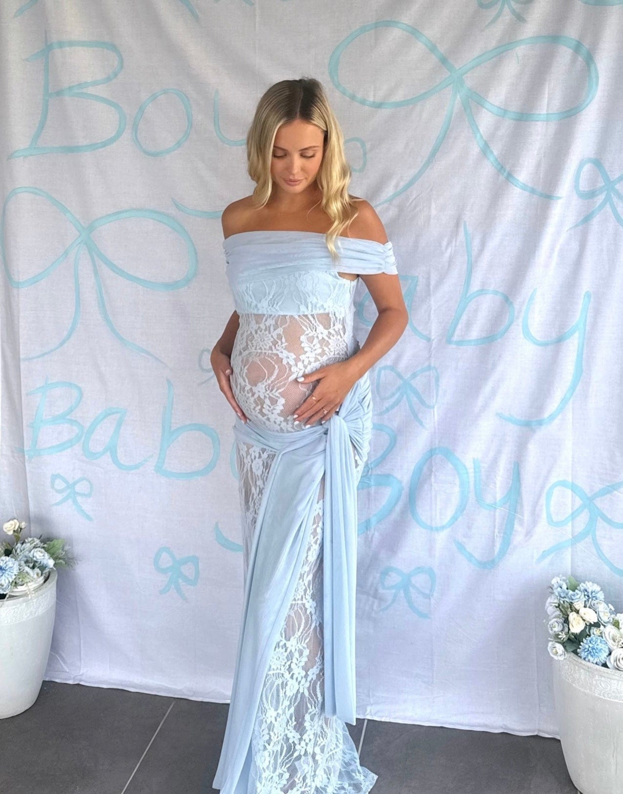 Pregnant woman wearing Everything Lace Hire Gracie Twist a lace maternity Baby Shower dress standing in front of a Baby Boy Sign