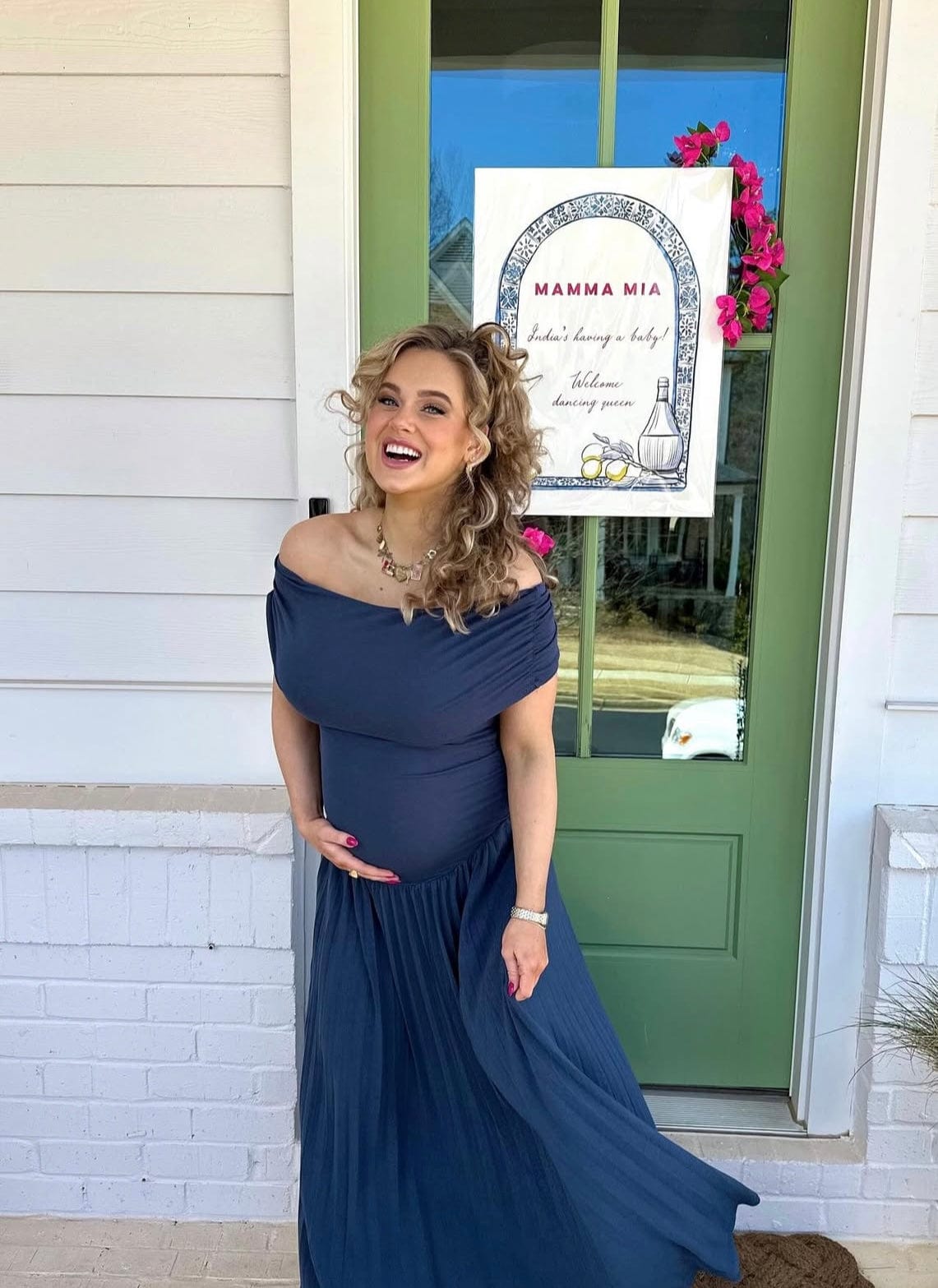 Pregnant mother cupping her bump during her Mamma Mia Baby Shower wearing Everything Lace Hire Field of Dreams Baby Shower Dress in navy blue.