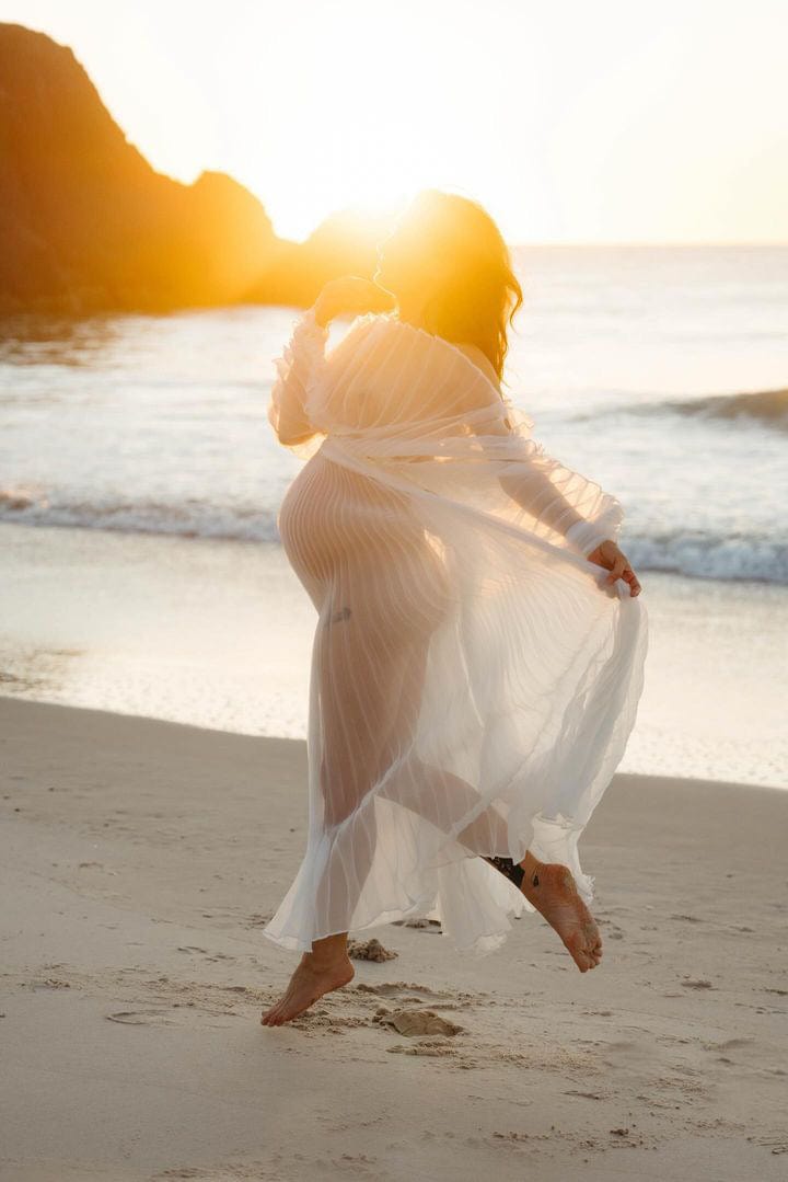 Beach sunrise maternity photoshoot with mum jumping into air wearing Everything Lace Hire Maternity Photoshoot Dress