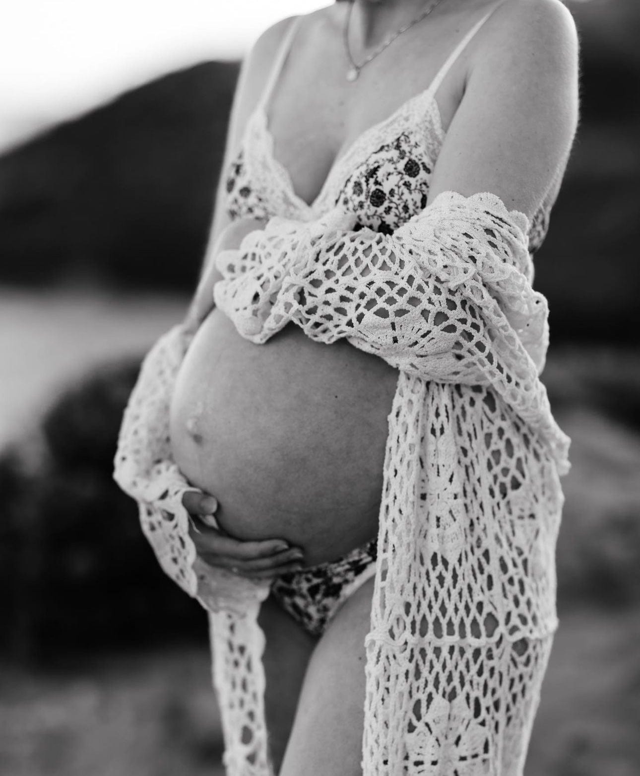 A pregnant lady wraps her arms around her bump wearing Everything Lace Hire Belle Maternity Crochet Robe