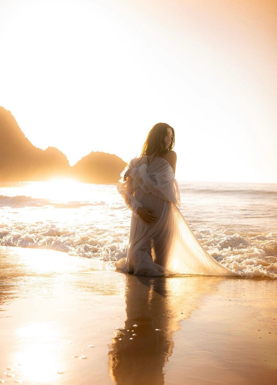 Beach maternity photoshoot on the beach wearing Everything Lace Hire Camille White Maternity Photoshoot Dress as she holds her pregnant belly