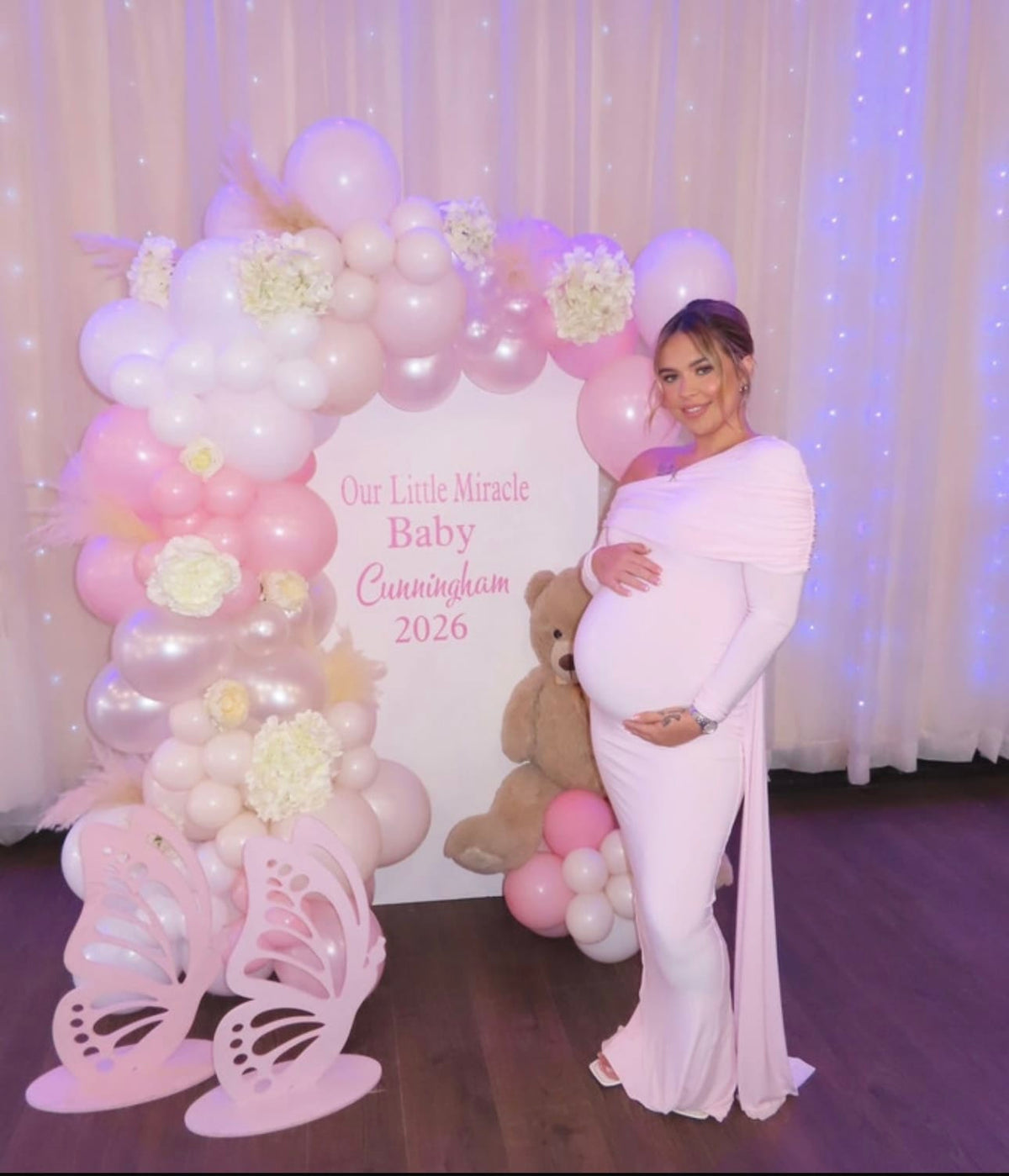 A pregnant woman wearing Everything Lace Hire Club L London Amara dress a long light pink maternity dress to celebrate her Baby Shower