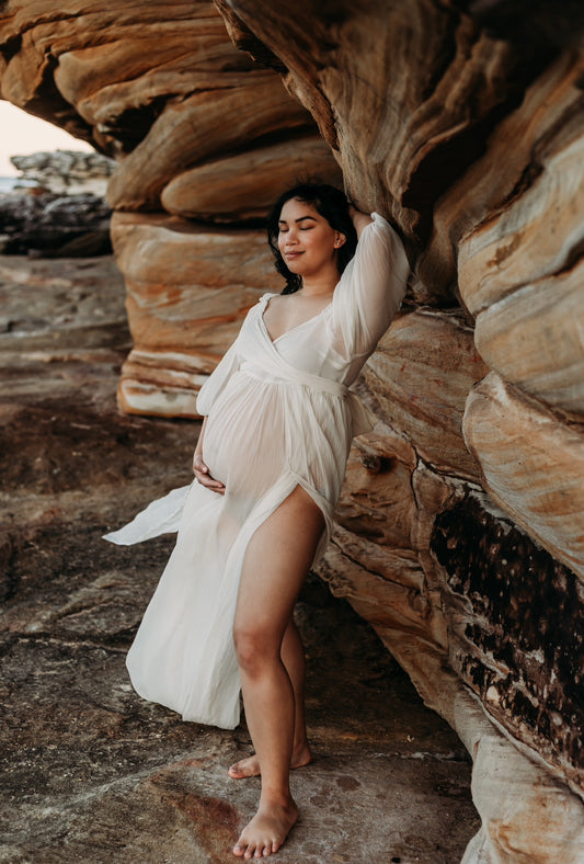 pregnant lady standing amongst the rocks with her arms in the air wearing Everything Lace Hire Co & Ry Illoura Gown