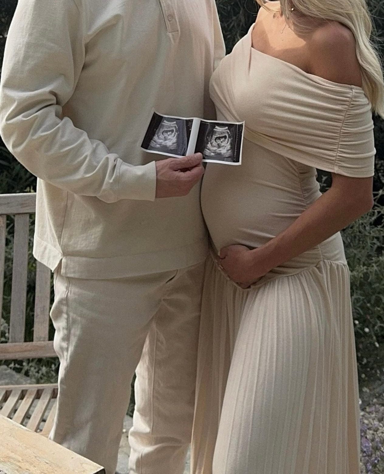 A pregnant lady wearing Everything Lace Hire Field Of Dreams Maternity Dress as she cups her pregnant belly next to her husband as they hold their baby scan picture