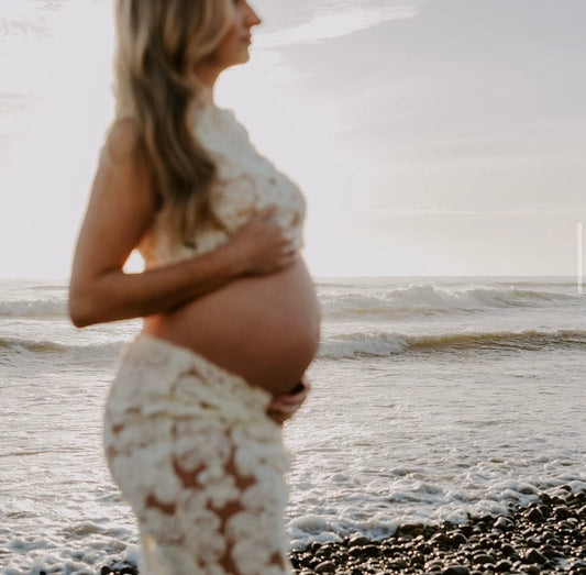 Pregnant woman in Everything Lace Hire Fiorella Set showcasing her pregnancy bump standing on a beach with waves in the background