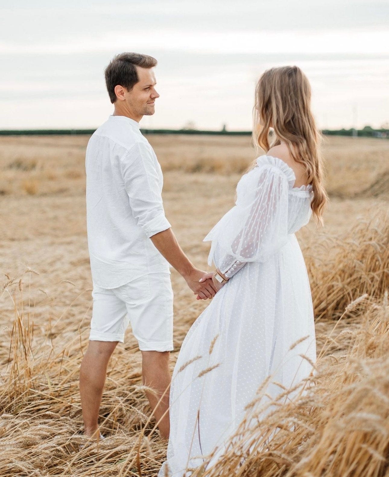 couple standing in a field looking at each other wearing Everything Lace Hire Anyutas Couture Grace dotted tulle maxi maternity photoshoot dress