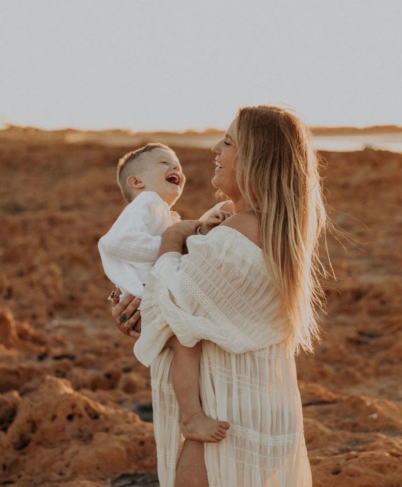 Maternity Photoshoot at the beach holding her son while wearing Everything Lace Hire Anabelle Maternity Photoshoot Dress