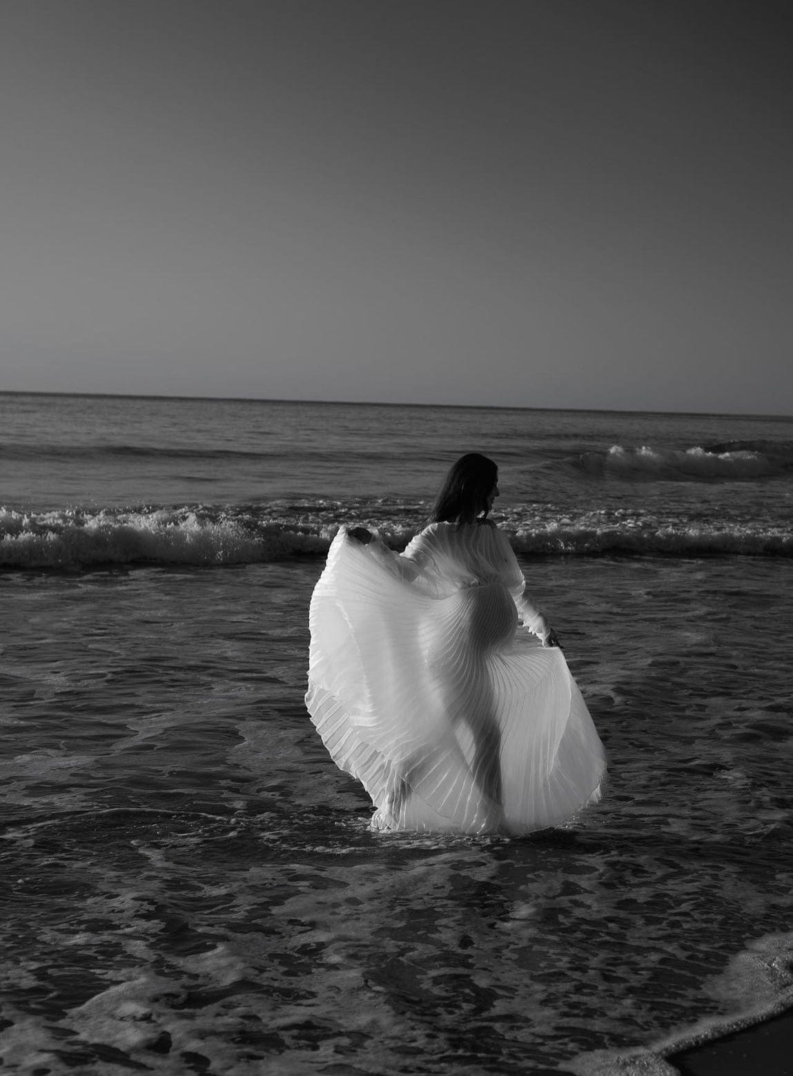 Mum to be running through the water holding Everything Lace Hire Camille photoshoot dress corners