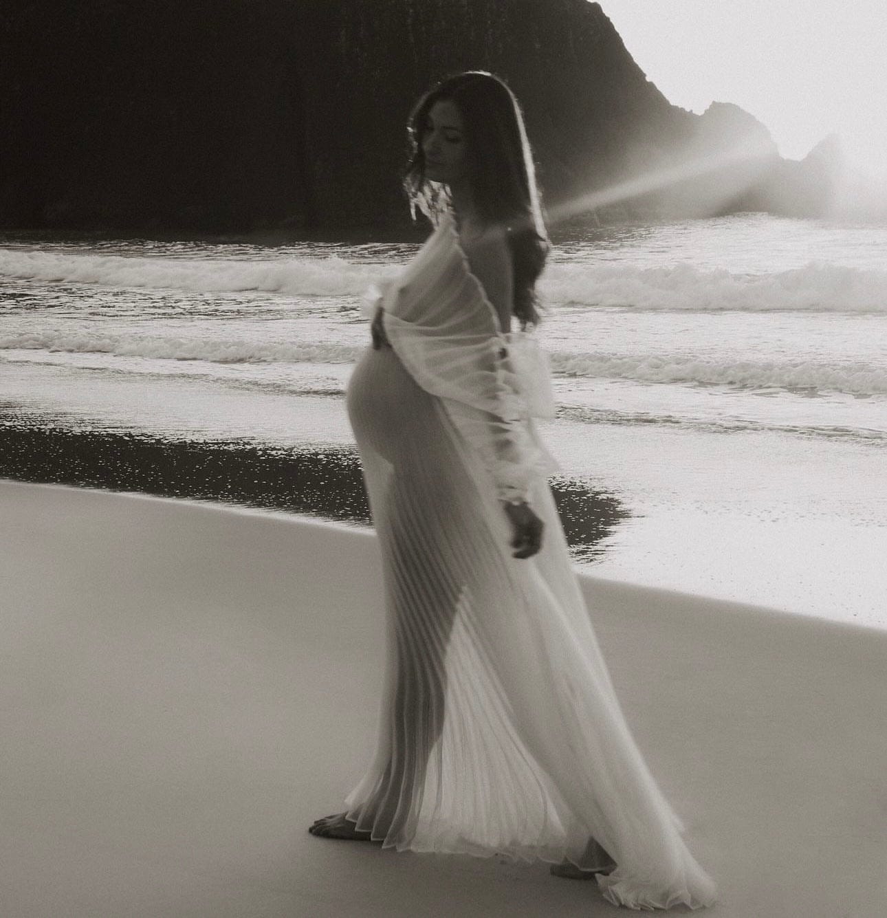 Mother to be walking along the beach wearing Everything Lace Hire Camille Maternity Photoshoot Dress
