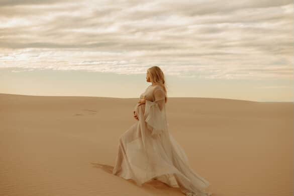 Woman in the Minna Gown from Everything Lace Hire a long flowing dress standing in a desert landscape with a cloudy sky.