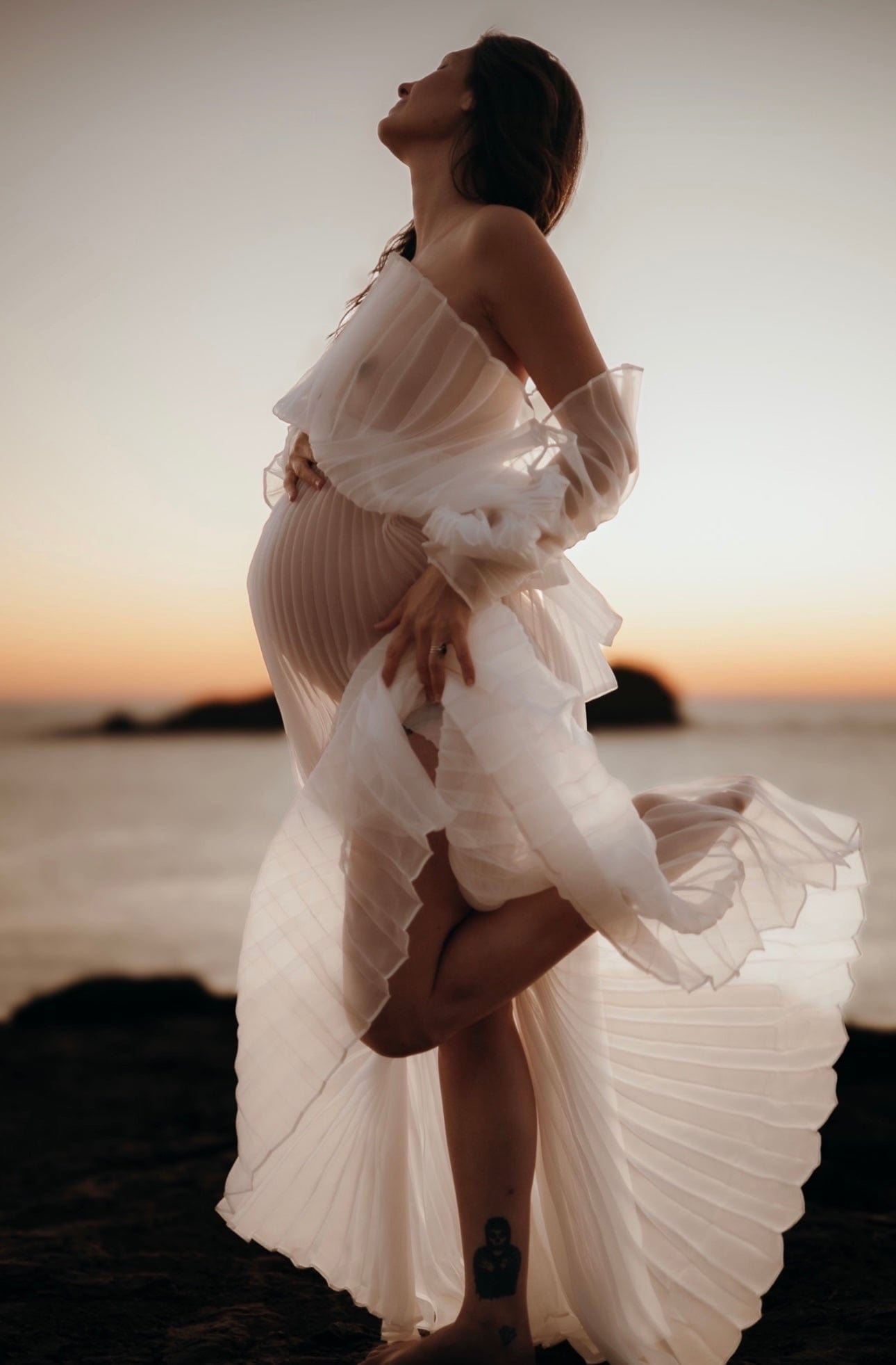 mum to be standing on one leg holding bump looking into the sky while wearing Everything Lace Hire Camille Maternity Photoshoot Dress