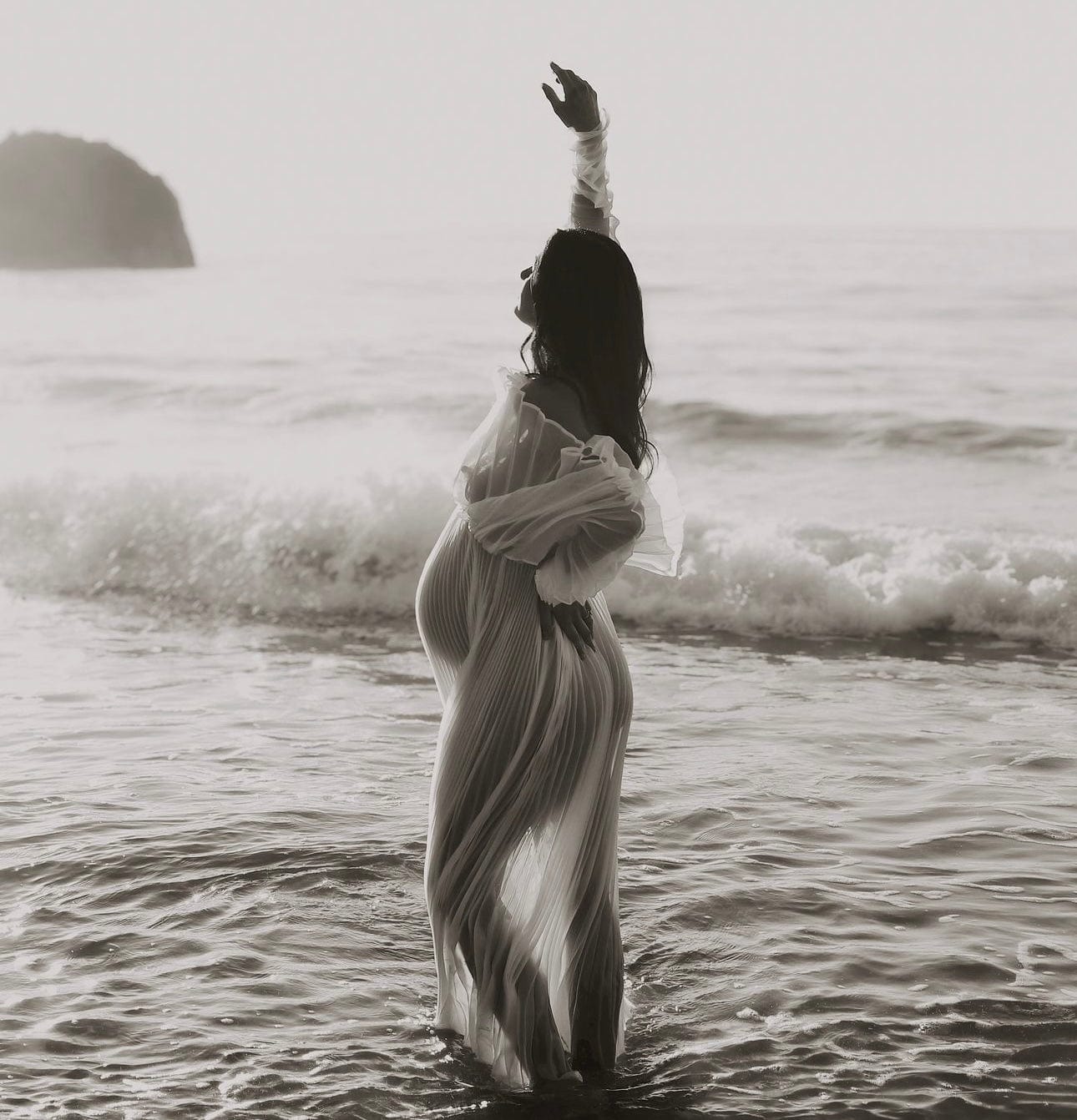 Beach maternity photoshoot standing in the sea with arms up wearing Everything Lace Hire Camille Maternity Photoshoot Dress.