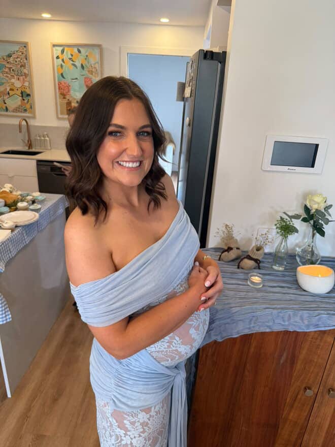 Pregnant lady wearing Everything Lace Hire Gracie Twist Baby Shower Dress a light blue lace dress standing in amongst her baby shower decorations.