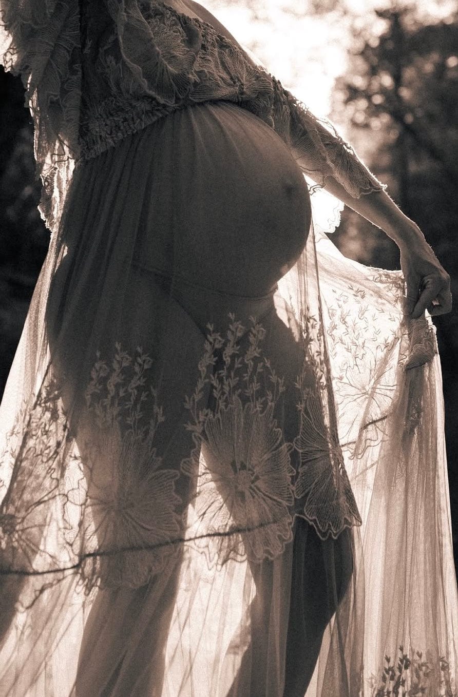 A beautiful close up image of a pregnancy lady bump during her maternity photoshoot wearing Everything Lace Hire Reclamation Euphoria Off the Shoulder Dress in rust