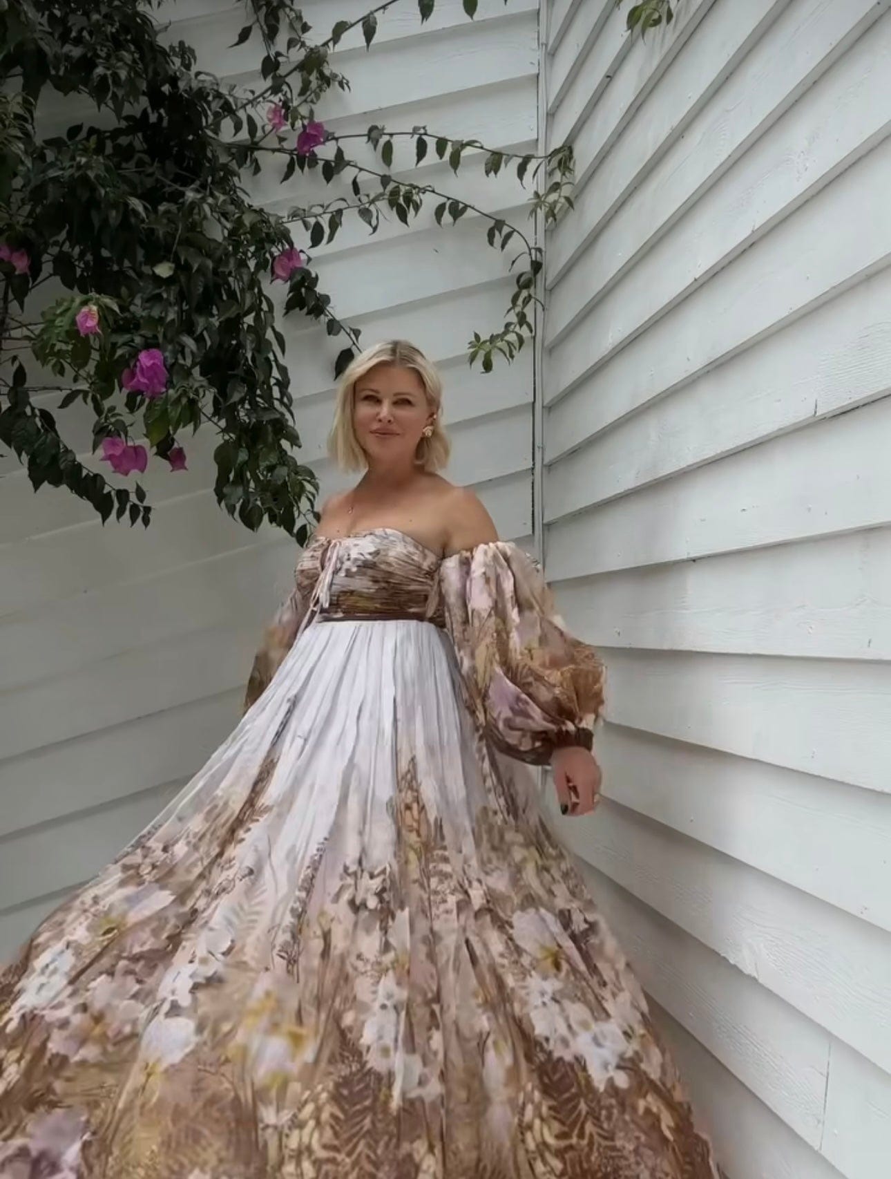 A lady standing among flowers wearing Everything Lace Hire Rooh Bronte Botanica Dress a brown floral dress