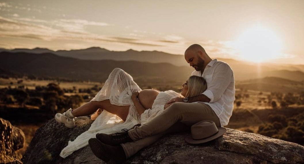 Couple lieing on a rock showcasing pregnancy wearing a ivory coloured chiffon two piece maternity photoshoot dress
